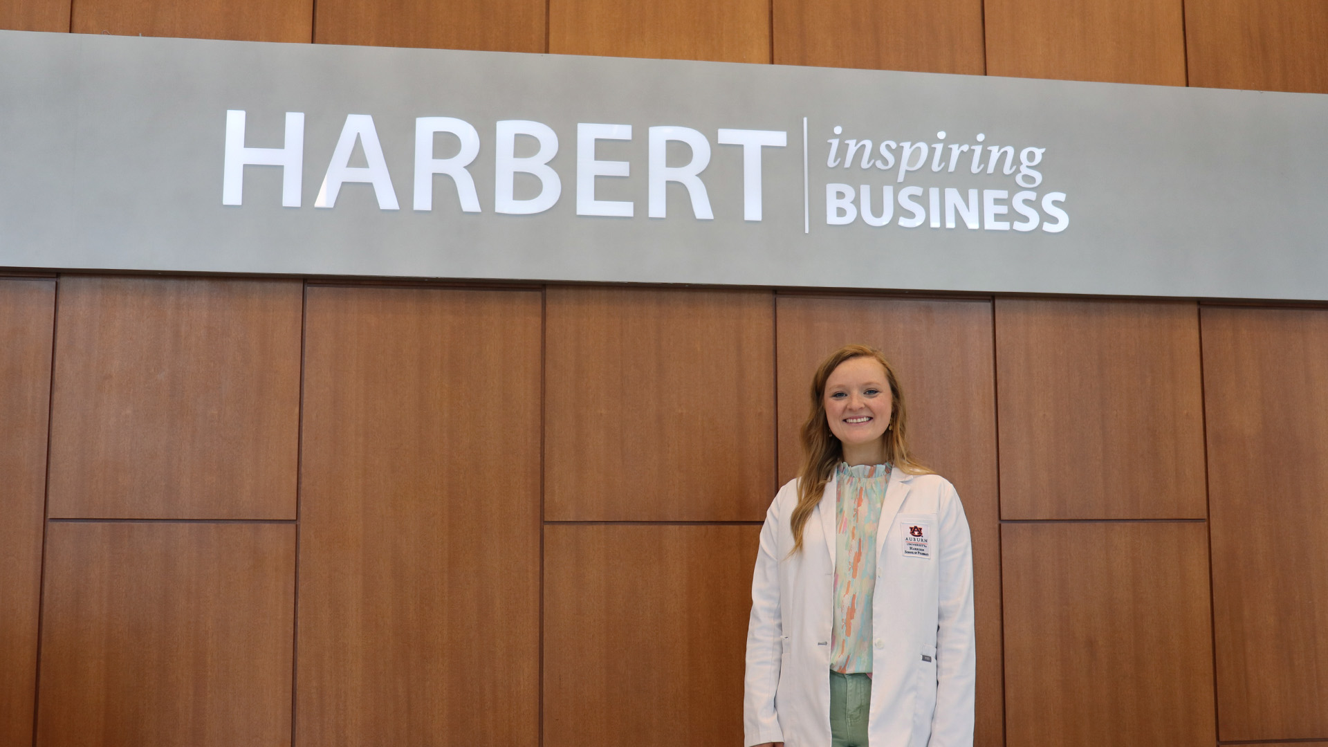 Student stands in white coat in front of college of business sign