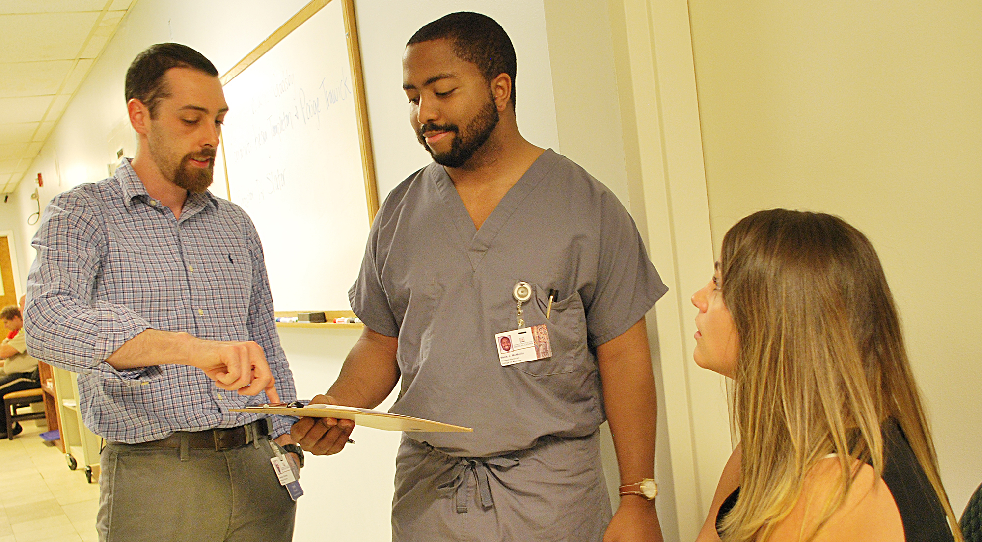 A pharmacy student and a medical student discuss a patient's chart while a faculty member observes