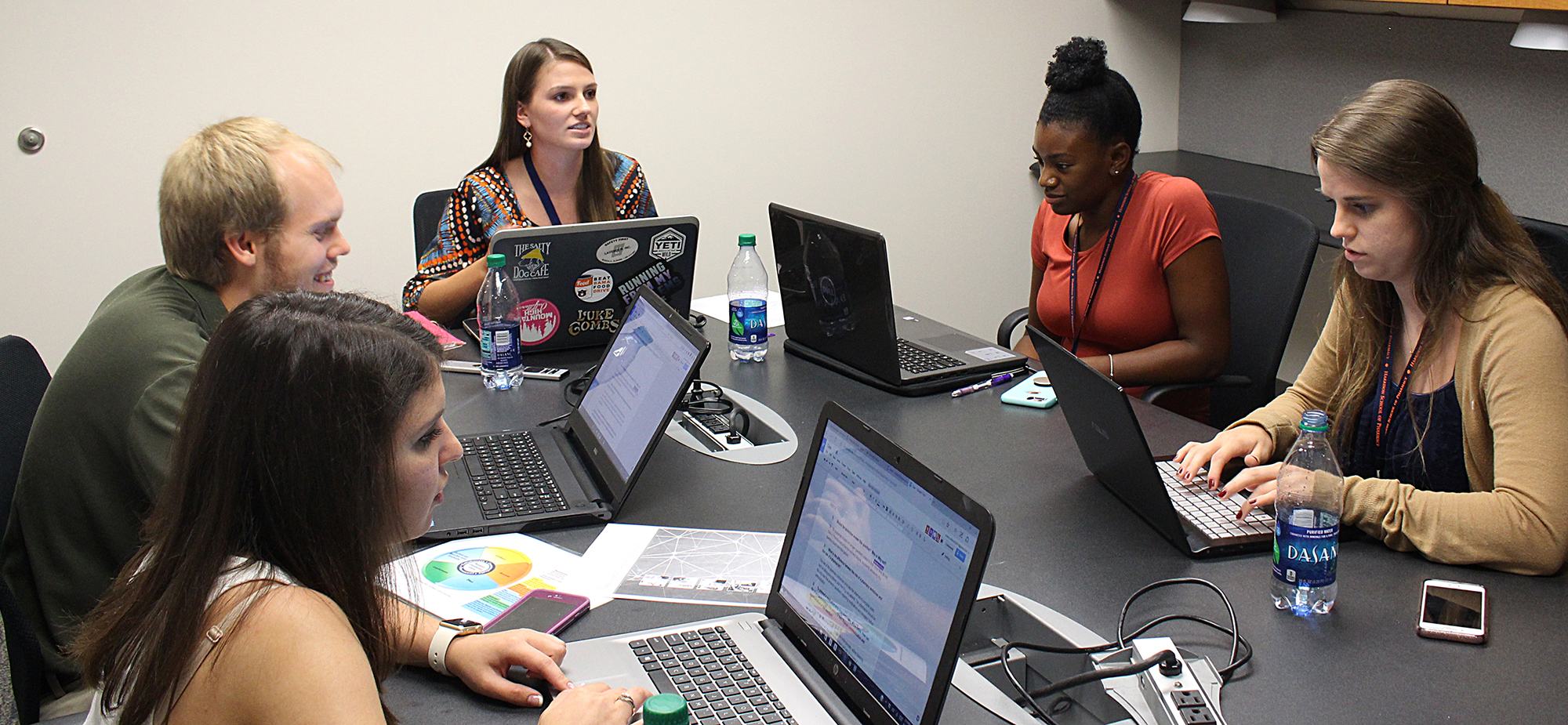 Pharmacy Students sit around a conference table with laptops, discussing work