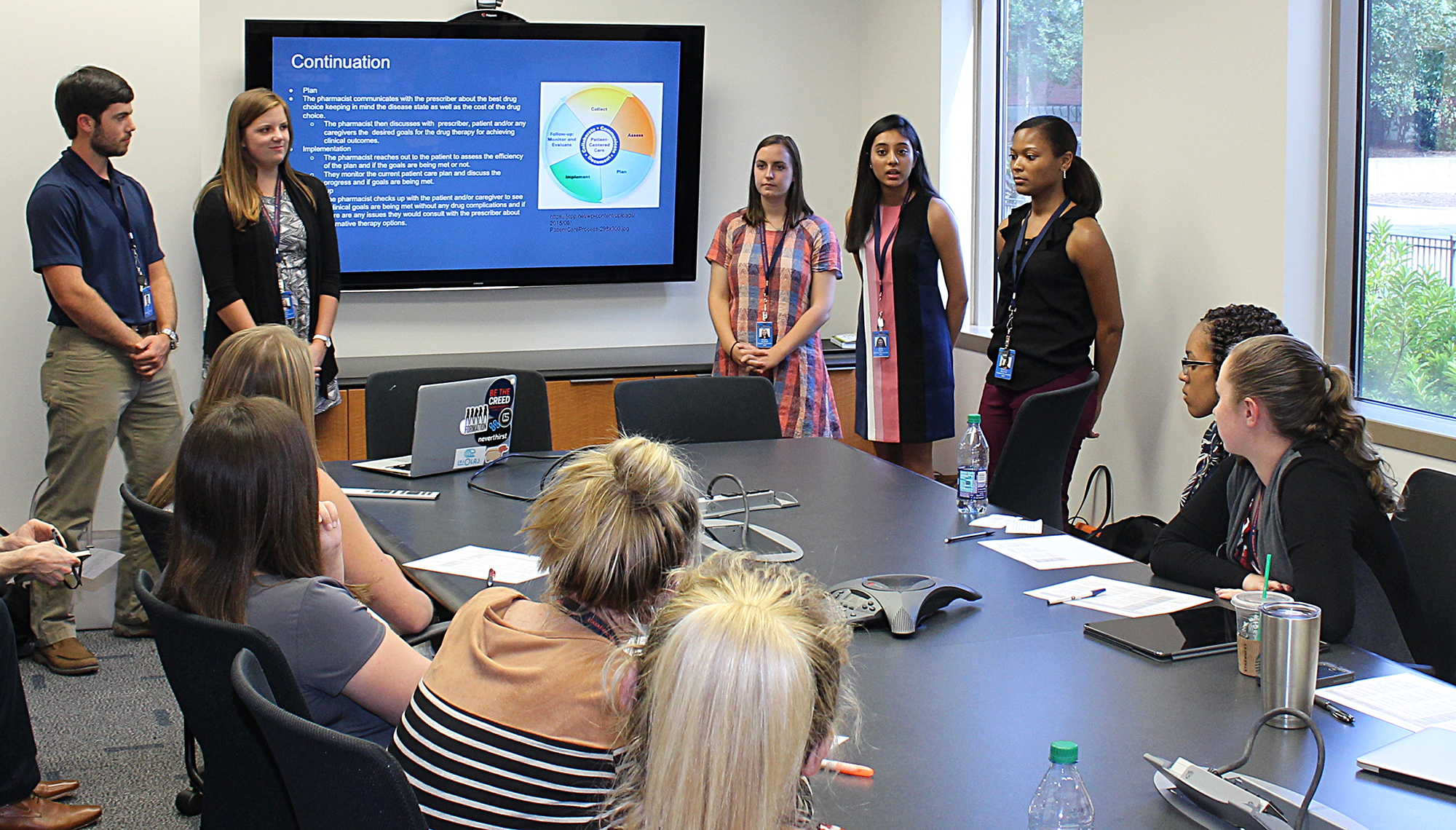 Pharmacy Students stand in front of a TV monitor, presenting to their classmates