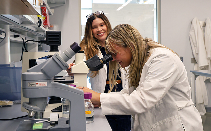 Student looks in microscope while faculty member watches