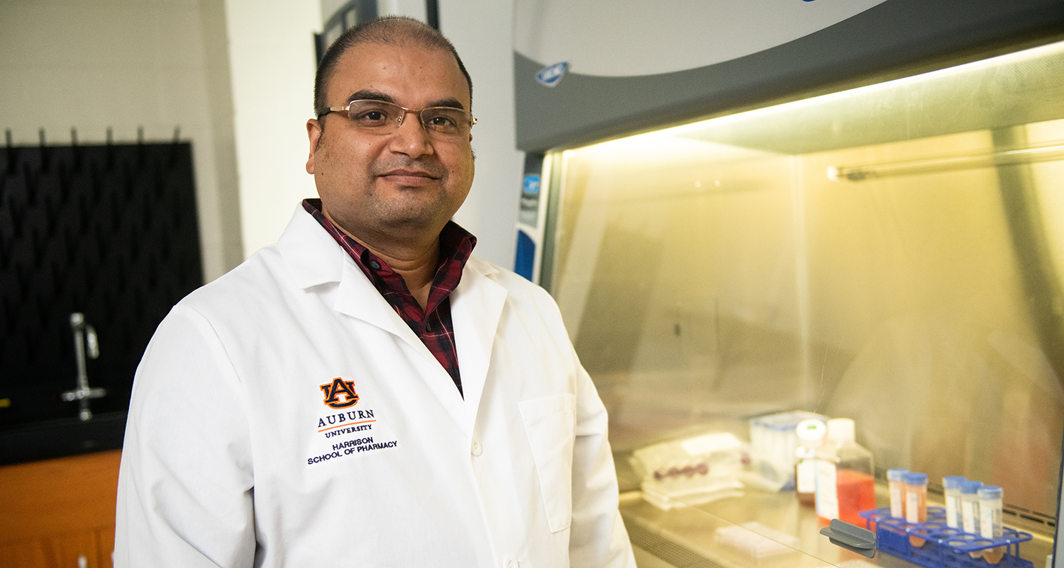 Dr. Mitra stands in front of vent hood in lab